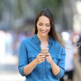Eine Frau auf einer belebten Straße schaut lächelnd auf ihr Smartphone