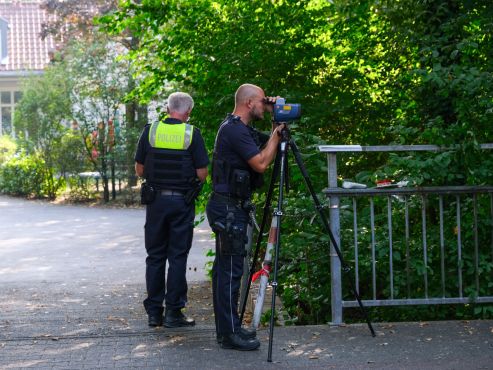 Ein Polizist führt eine Geschwindigkeitsmessung durch. Neben ihm steht mit dem Rücken zur Kamera ein weiterer Polizist