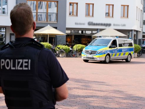 Ein Polizist von hinten, der in Richtung eines sich nahenden Streifenwagens blickt
